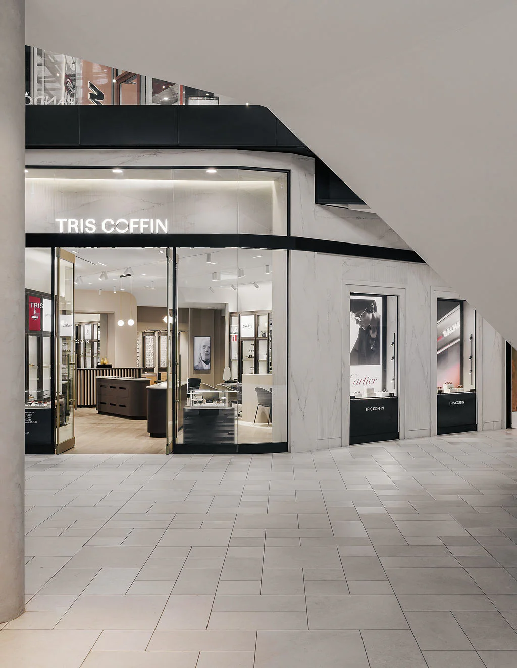 A modern jewelry store named Tris Coffin with large glass windows and doors, bright interior lighting, display cases, and stylish decor, located in a shopping mall with tiled floors.
