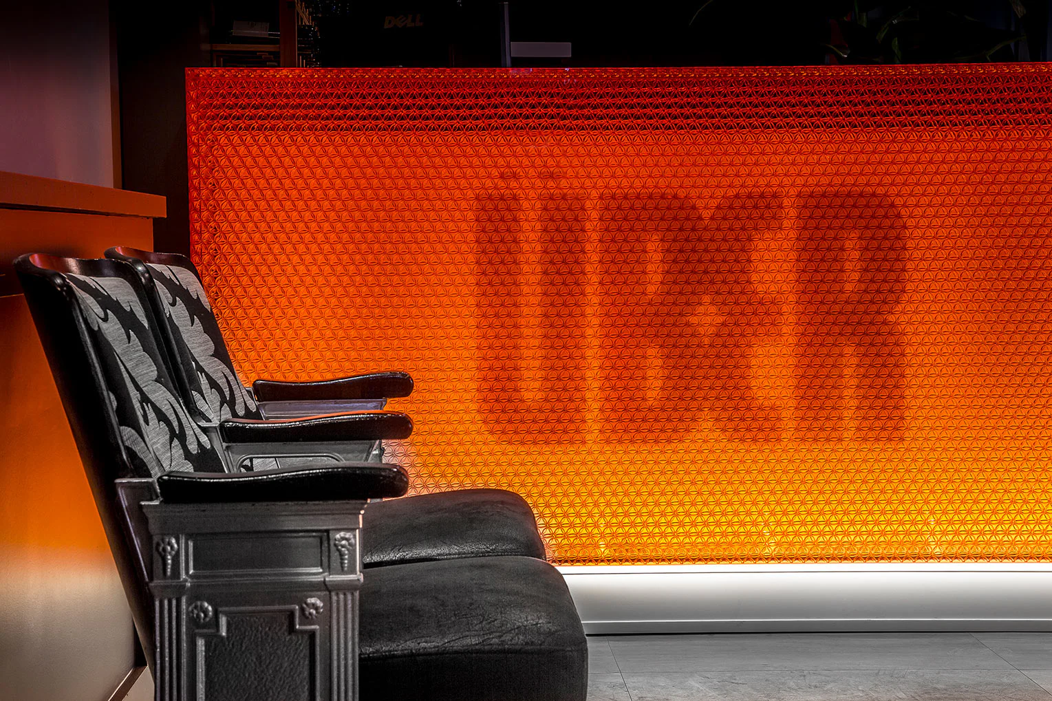 Three black upholstered chairs sit beside an orange, honeycomb-patterned wall with the word "UBER" visibly illuminated in large letters.